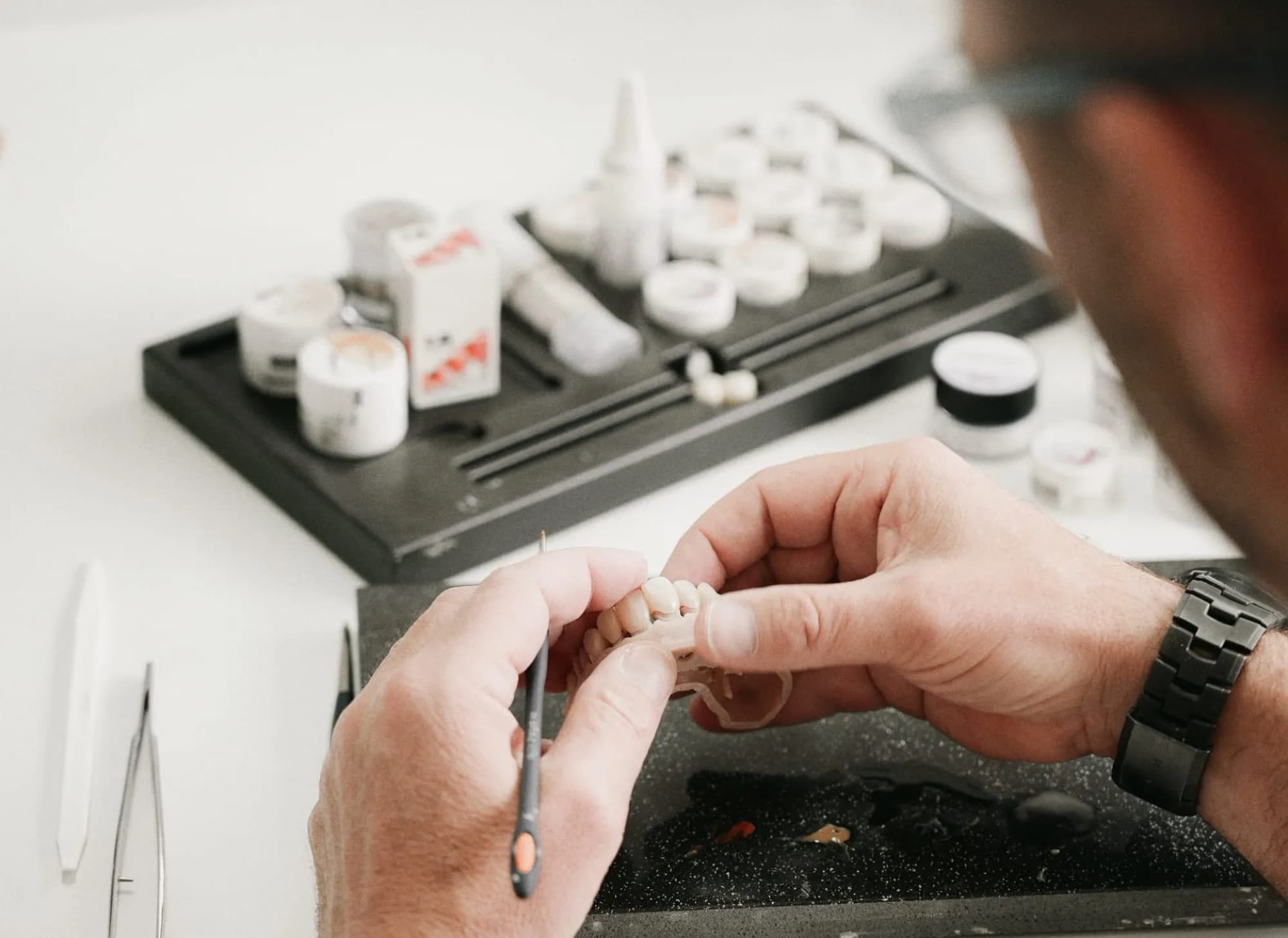 A dental technician's hands finishing a restoration at the laboratory bench.
