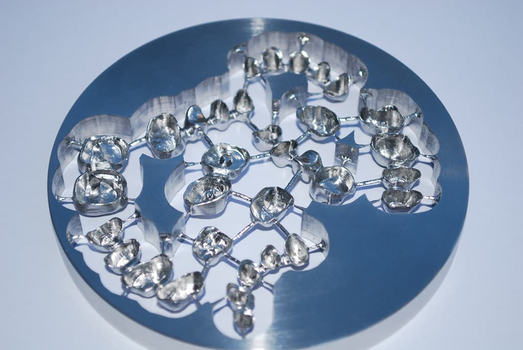 A milled titanium disc holding a batch of implant substructures still attached by support struts.